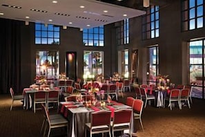 Un salón de banquetes con varias mesas dispuestas para comer, amplias ventanas y un techo alto.