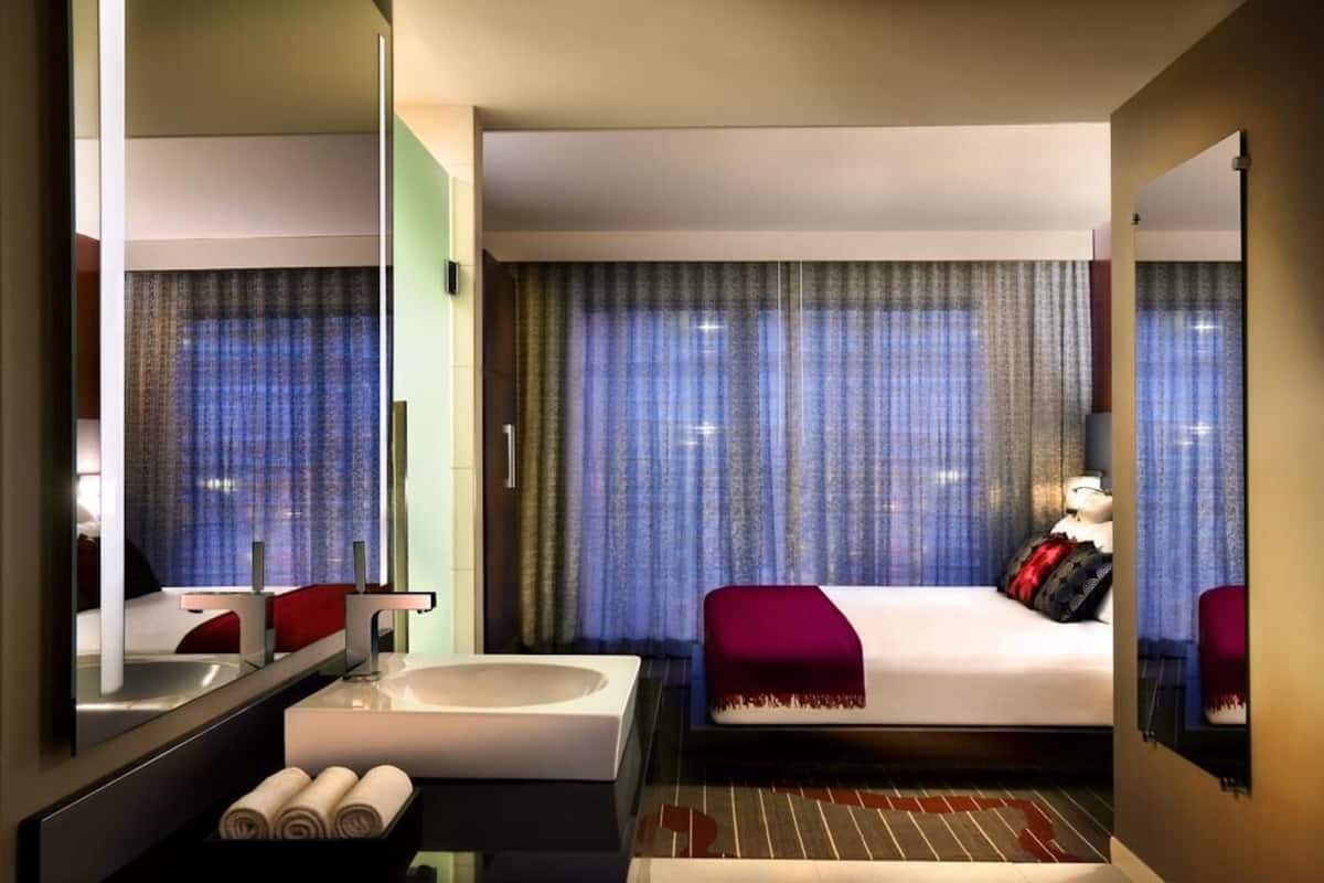 Una habitación de hotel con una cama grande, una bañera blanca, un espejo y una ventana con cortinas.