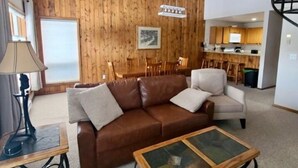 Een moderne woonkamer met een bruine leren bank, een glazen salontafel en een houten eettafel.