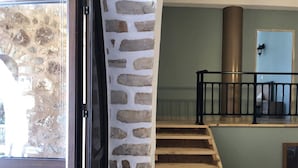 Eine Treppe mit Holzbodenstufen führt zu einer Zwischenebene, an einer Steinwand entlang mit einem Metallgeländer.