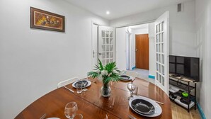 A dining area with a wooden table set for four, a vase with flowers, and a television on a stand. - Chic apart with parking (Mantes-la-Jolie)