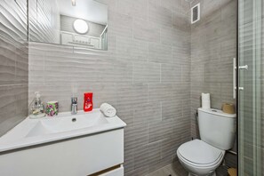 Une salle de bain avec un lavabo blanc, un miroir, des toilettes et un espace douche.