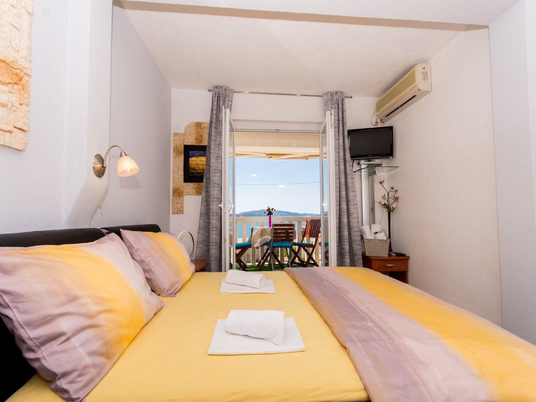 A hotel room with a bed, a TV, and a balcony with a table and chairs.