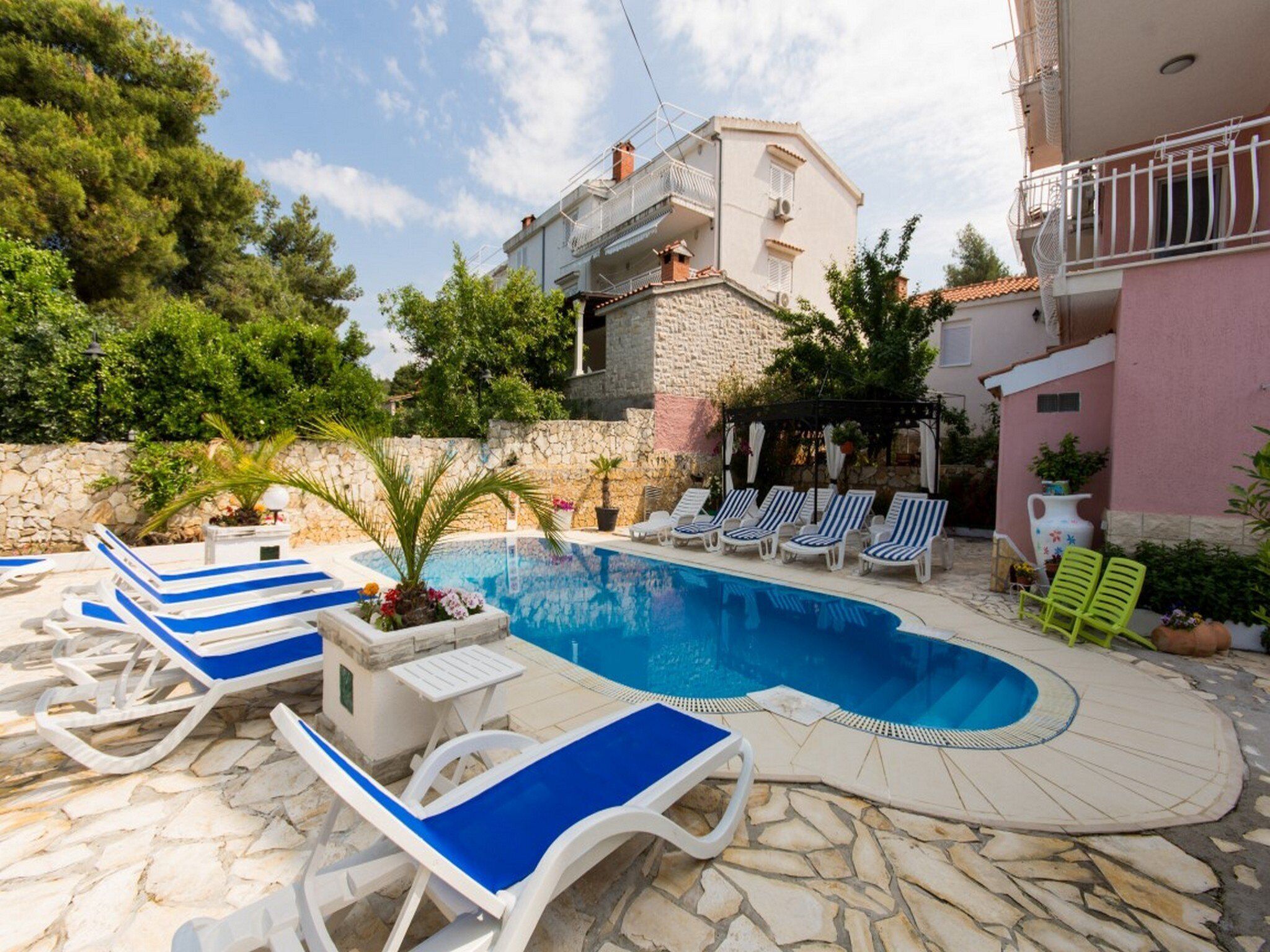 Un espace piscine avec des chaises longues, un palmier et un mur en pierre.
