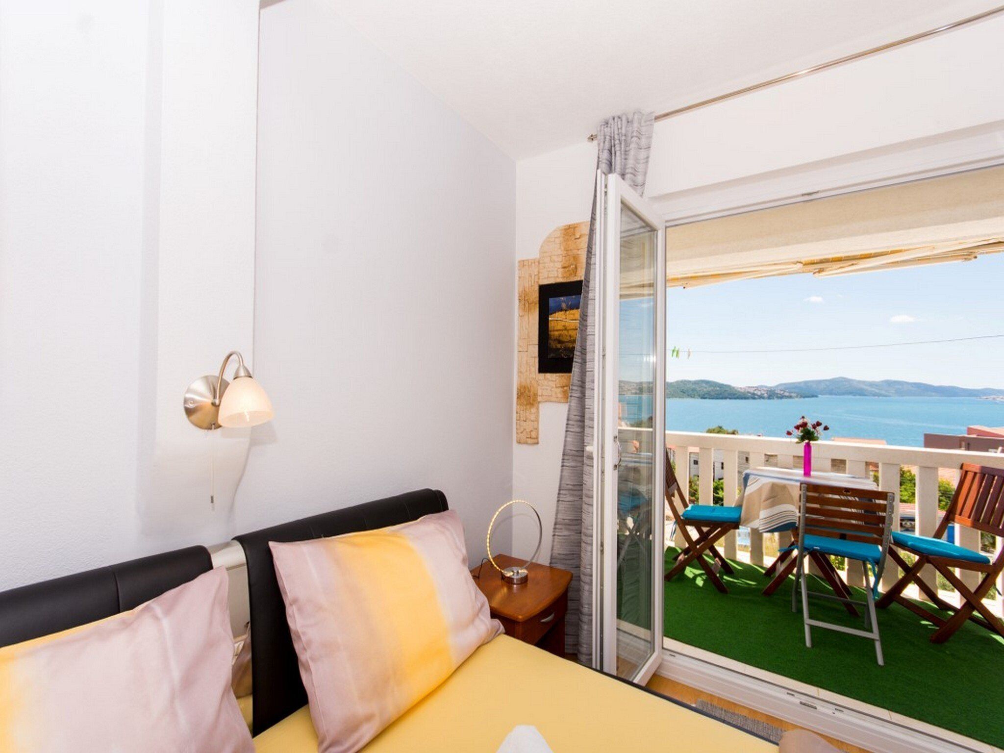 A balcony with a view of the sea, a bed with a headboard, and a table with chairs.