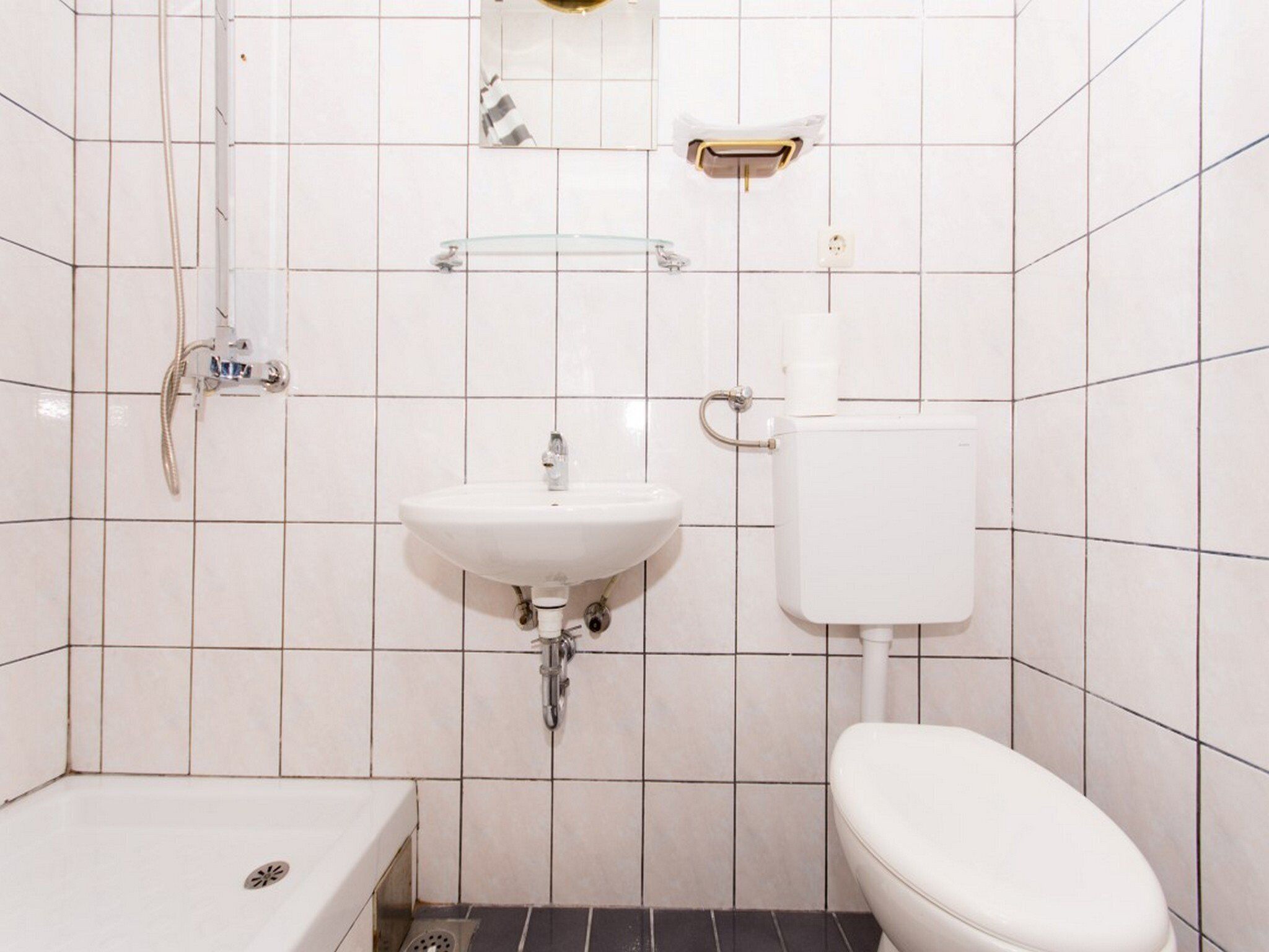 A small, clean bathroom with white tiles, a white sink, a toilet, and a shower.