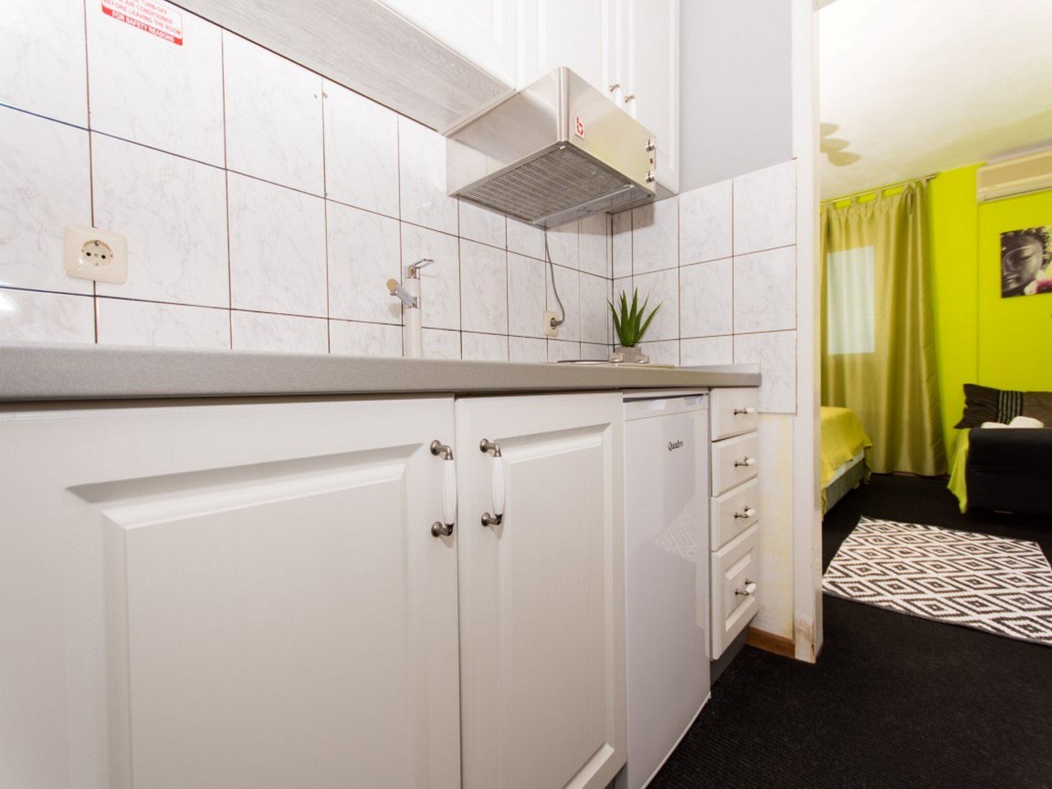 Una cocina compacta con armarios blancos, estufa integrada y una pequeña planta en maceta.