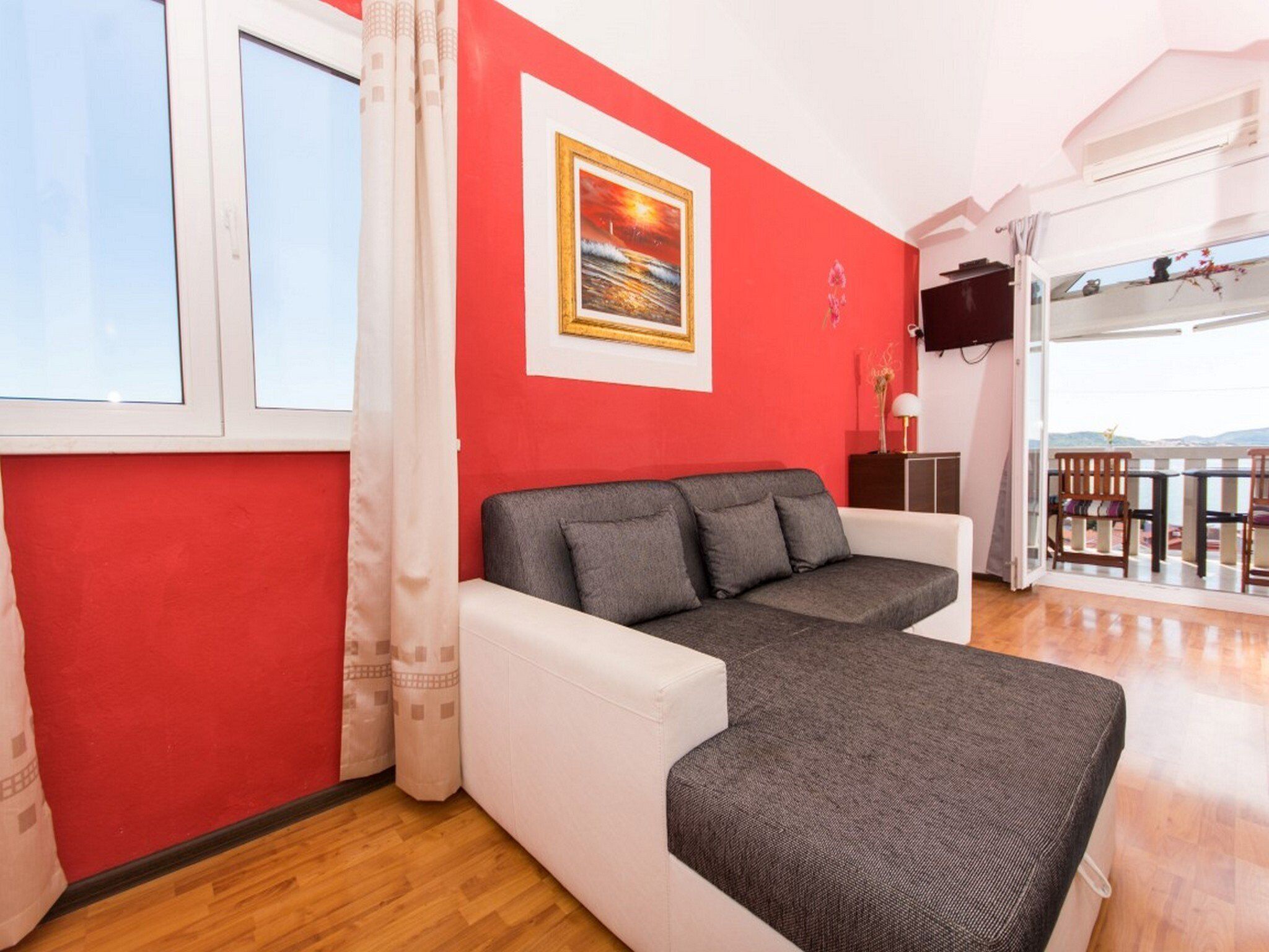Una sala de estar con una pared roja, un sofá gris y una ventana con cortinas.