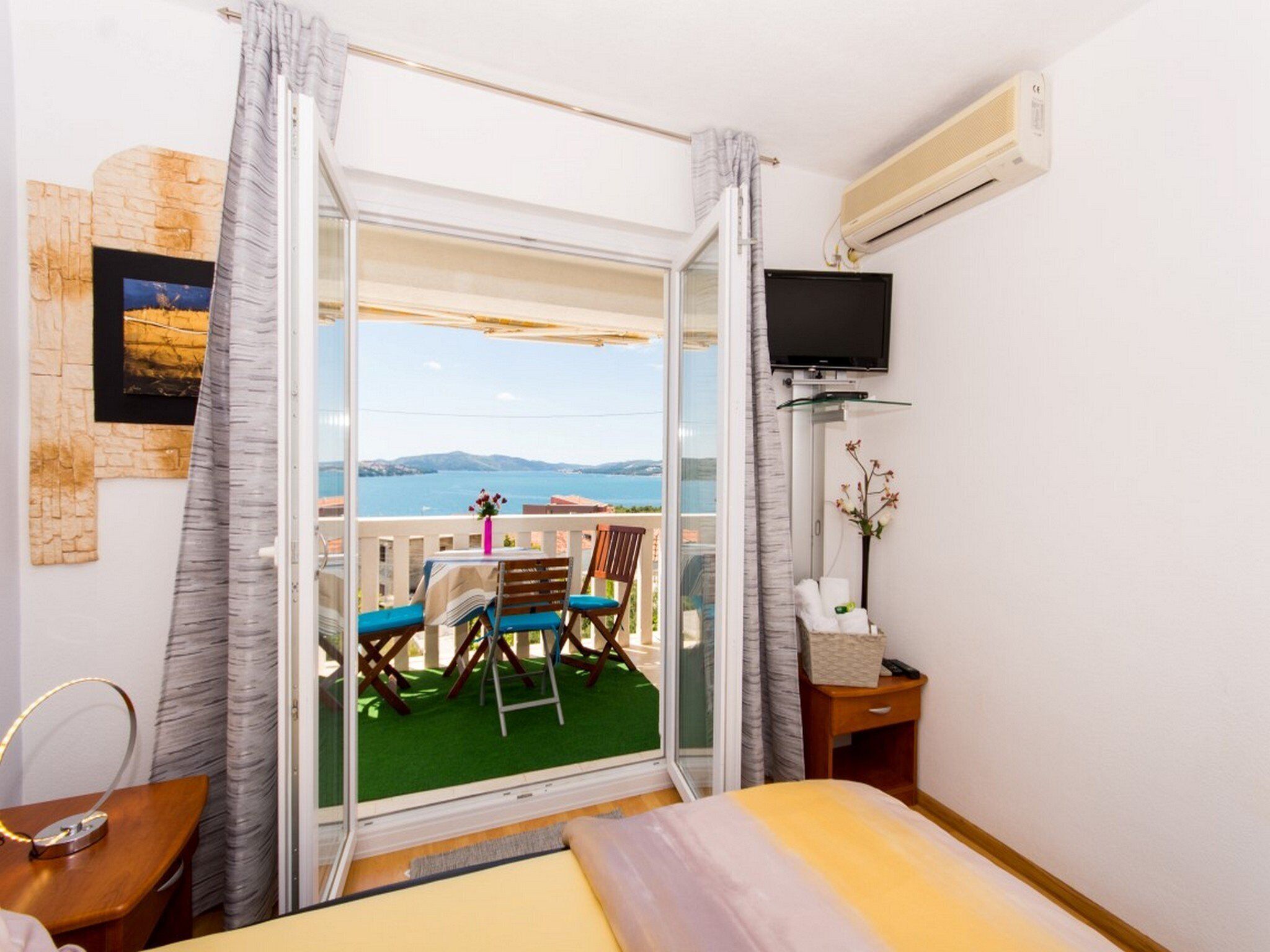 Habitación de hotel con balcón, cama, televisión y una mesita.