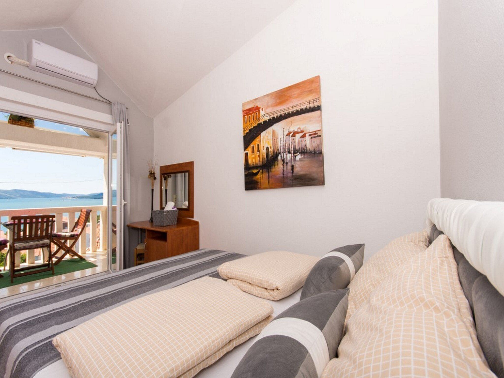 A hotel room with a bed, a desk, a chair, a painting, and a balcony with a view.