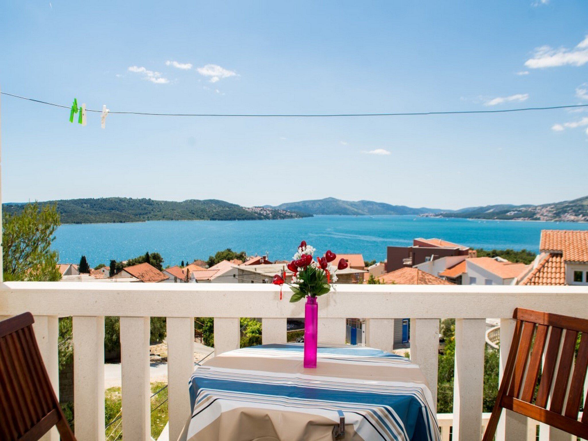 A balcony with a table, chairs, and a view of a lake and mountains.