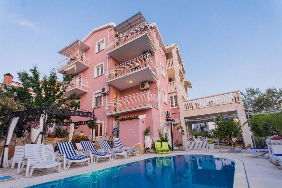 A multi-story pink building with balconies, a swimming pool, and lounge chairs.