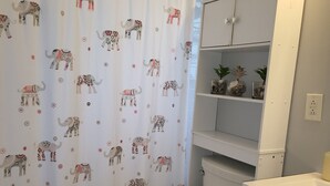 Een badkamer met een toilet, een douchegordijn met olifantmotieven en een kast met planken.