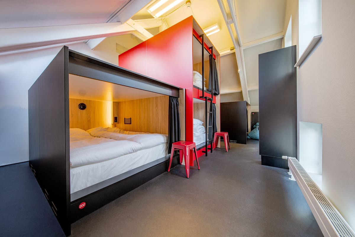 A modern hotel room with a bunk bed, a desk, and a red accent wall.