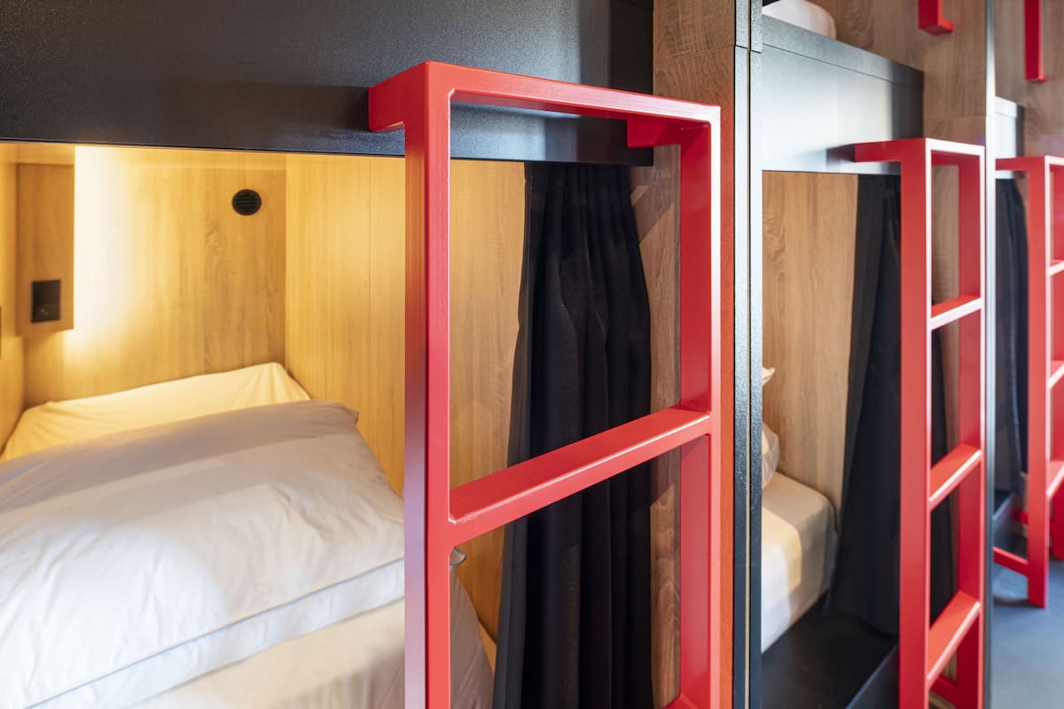A hotel room with a wooden headboard, a red-framed bed, and a black curtain.