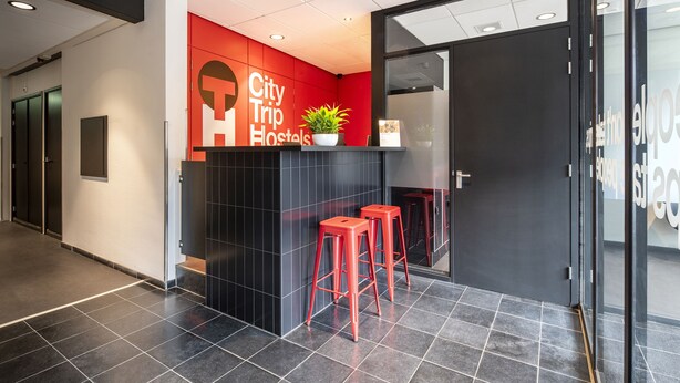 A reception area with a red accent wall, a black counter, and red stools. - City Trip Hostels (Purmerend)