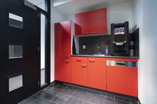 A modern kitchen with red cabinets, a dishwasher, and a coffee machine. - City Trip Hostels (Purmerend)