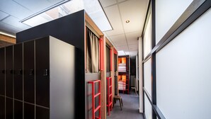 A corridor with lockers, red metal ladders, and a bed in the background. - City Trip Hostels (Purmerend)