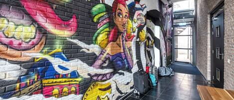 Un vestíbulo de hotel con un mural colorido en la pared, un mostrador de recepción de madera y un suelo de baldosas.