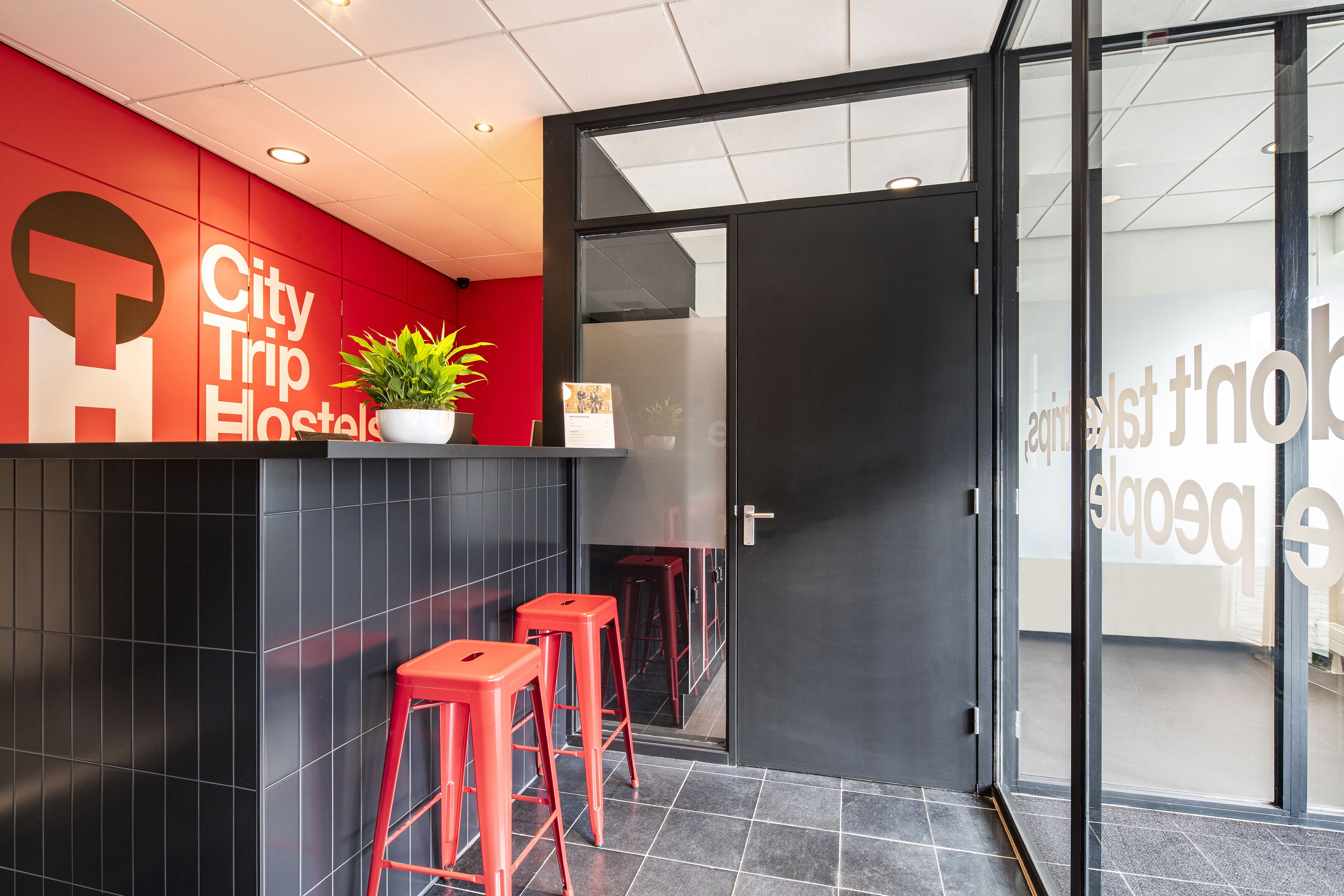 Un moderno vestíbulo de hotel con una pared de acento roja, una recepción y dos taburetes rojos de bar.
