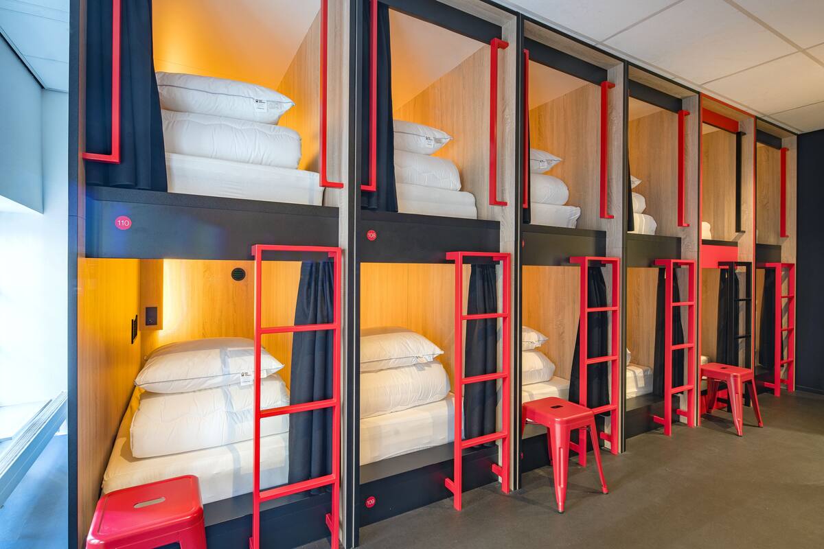 A hotel room with bunk beds, red ladders, and small red stools.