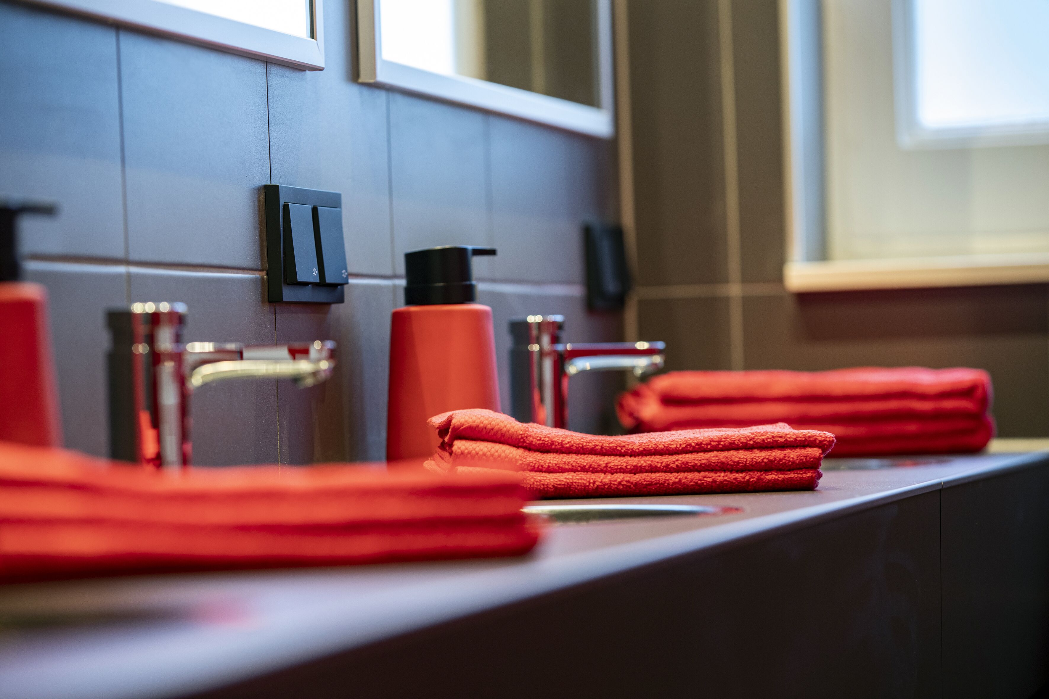 Un baño de diseño moderno, con un lavamanos, una toalla roja y un dispensador de jabón negro.