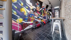 A room with a colorful mural on the wall, a staircase, and a table with stools. - City Trip Hostels (Purmerend)