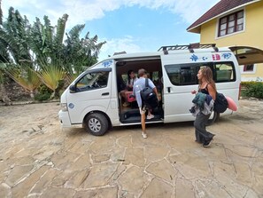 A white van parked on a stone pavement with its back door open, revealing passengers inside. - Maranda Cool Breeze Villa - 2minutes to the beach (Kwale County)