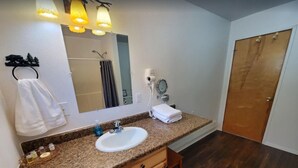 A bathroom with a granite countertop sink, wooden cabinets, a mirror, a hairdryer, and a towel rack. - {Forget-Me-Not Inn} Alaskan Vacation Rental (Bear Suite) (Sitka)
