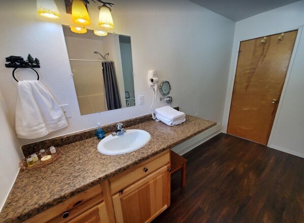 A bathroom with a granite countertop sink, wooden cabinets, a mirror, a hairdryer, and a towel rack. - {Forget-Me-Not Inn} Alaskan Vacation Rental (Bear Suite) (Sitka)