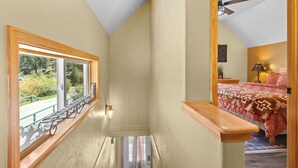 Un escalier étroit mène à une chambre à coucher qui contient un lit, une table de chevet et une fenêtre donnant sur un paysage verdoyant.