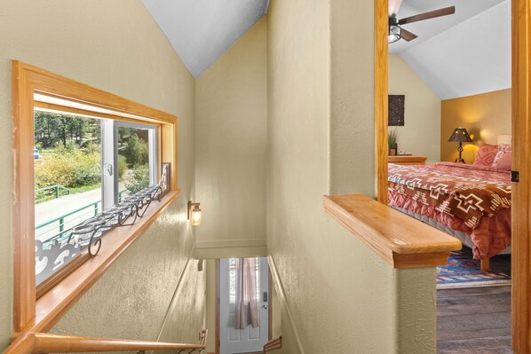 A narrow staircase leading to a bedroom with a bed, a nightstand, and a window with a view of greenery. - On the River "River Retreat Southwest Cabin #1" In Town, Remodeled, Pet Friendly (Red River)