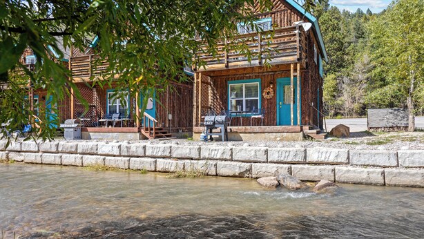 Un chalet rustique doté d’une véranda, d’un barbecue et offrant une vue sur une rivière.