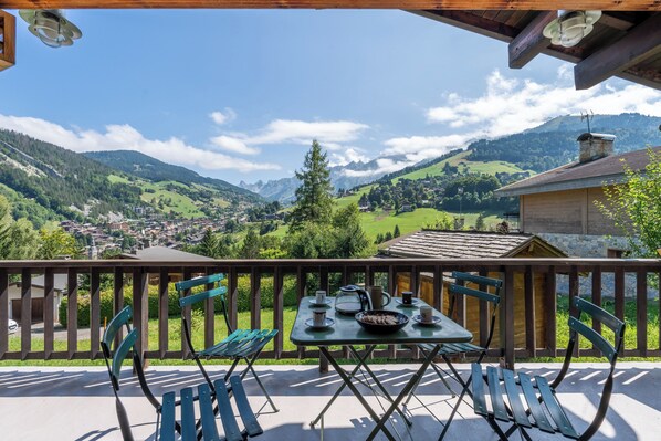 A balcony with a table set for dining, overlooking a mountainous landscape.