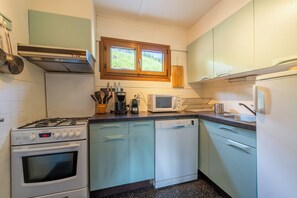 A compact kitchen with a gas stove, oven, microwave, dishwasher, and a window with a view of greenery.