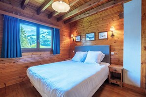 A wooden cabin bedroom with a large bed, a nightstand, and a window with curtains.