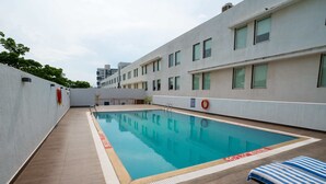 A rooftop swimming pool with a clear blue water surface, surrounded by a tiled deck and a white building with multiple windows. - Hotel Halez (Chennai)