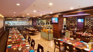 A restaurant with multiple dining tables, a bar area, and a television screen. - Hotel Halez (Chennai)
