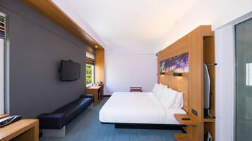 Una habitación de hotel moderna con una cama grande, un escritorio con silla, un banco y un televisor montado en la pared.