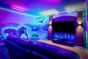 A room with a large flat-screen TV, a leather sofa, and a wall mural of a dragon and mountains. - Kids Bunk Themed Bedrooms | Theater Room | Private Pool with Golf Course Views (Kissimmee)