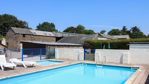 A rectangular swimming pool with clear blue water, surrounded by a white wall and a blue fence. There are two white lounge chairs and a metal gate leading to a covered area. - The Corn Tallet (Bideford)