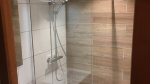 Ducha con grifo cromado y ducha de mano, paredes de azulejos y una pared decorativa de madera.