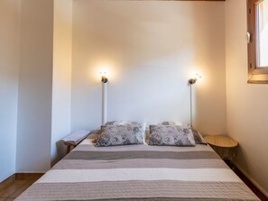Un dormitorio con una cama, dos lámparas de pared, una mesita redonda y una mesita de noche.