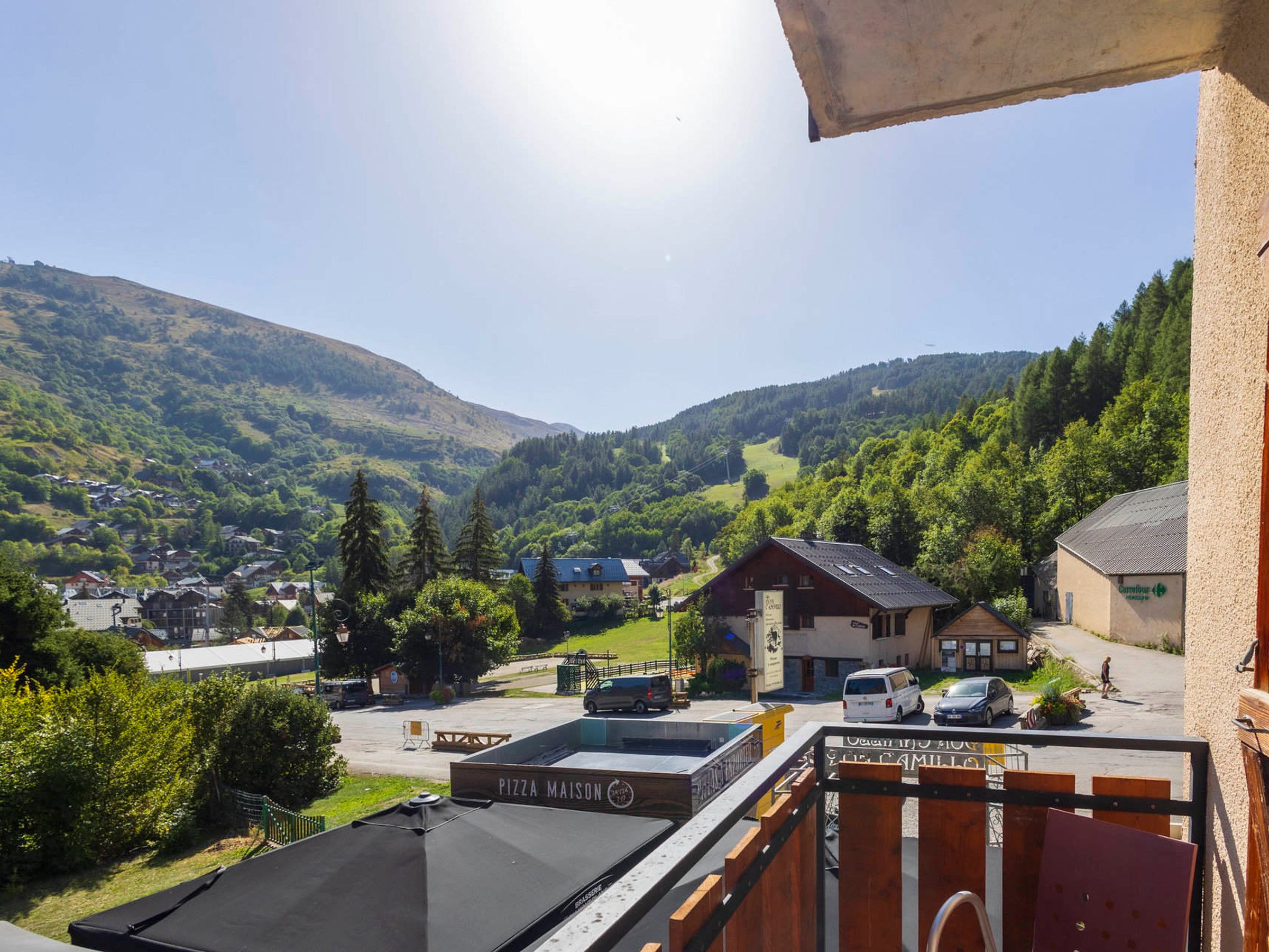 Udsigt fra en balkon over et byområde med en pizzeria, et bjerg i baggrunden og en klar himmel.