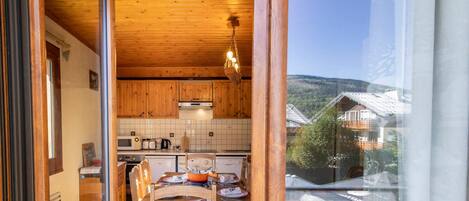 Un interior de madera con comedor, cocina y vistas a través de un ventanal.