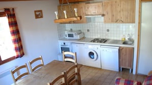 Una cocina compacta con armarios de madera, microondas, lavadora y comedor con mesa y sillas de madera.
