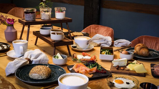 A wooden dining table with various breakfast items including bread, eggs, cheese, and smoked salmon. - Himmelreich Braunfels (Braunfels)