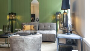 A modern living room with a grey sofa, ottoman, and a glass coffee table. There is a floor lamp and a mirror on the wall. - Himmelreich Braunfels (Braunfels)