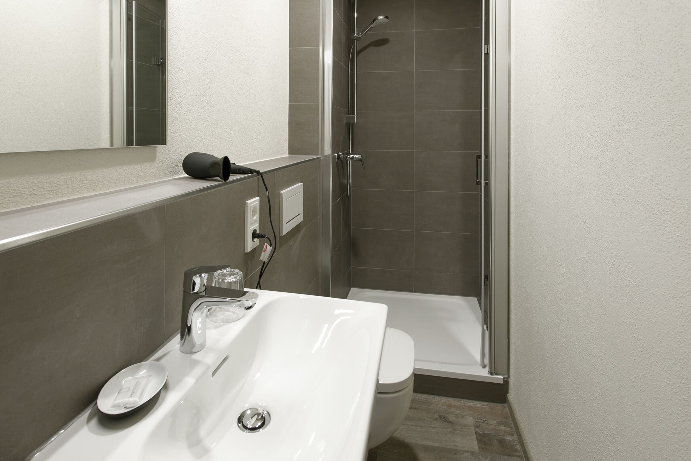 Un baño moderno con un lavamanos blanco, un espejo y una zona de ducha.