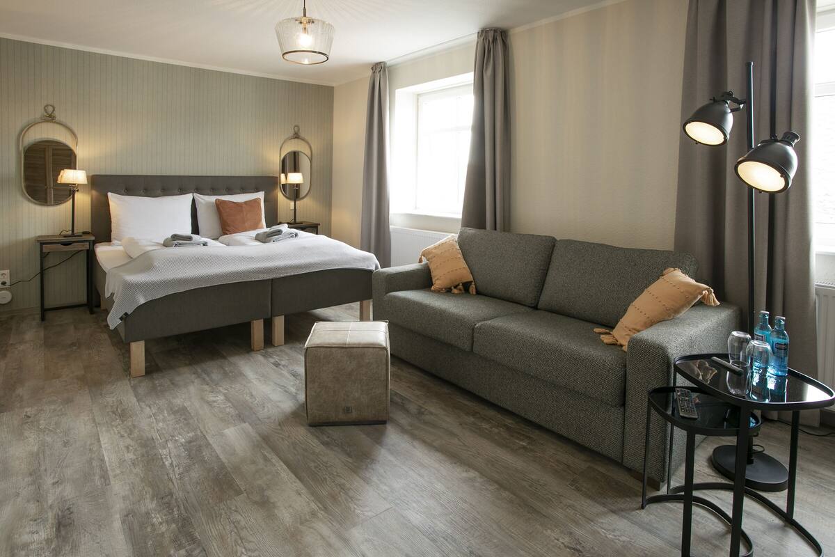 A hotel room with a bed, a sofa, a small table, and a lamp.